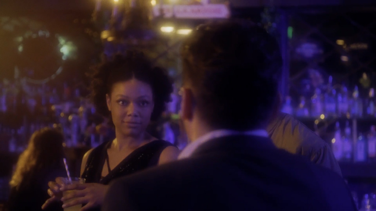 A man and a woman wearing formal attire look at one another in a nightclub